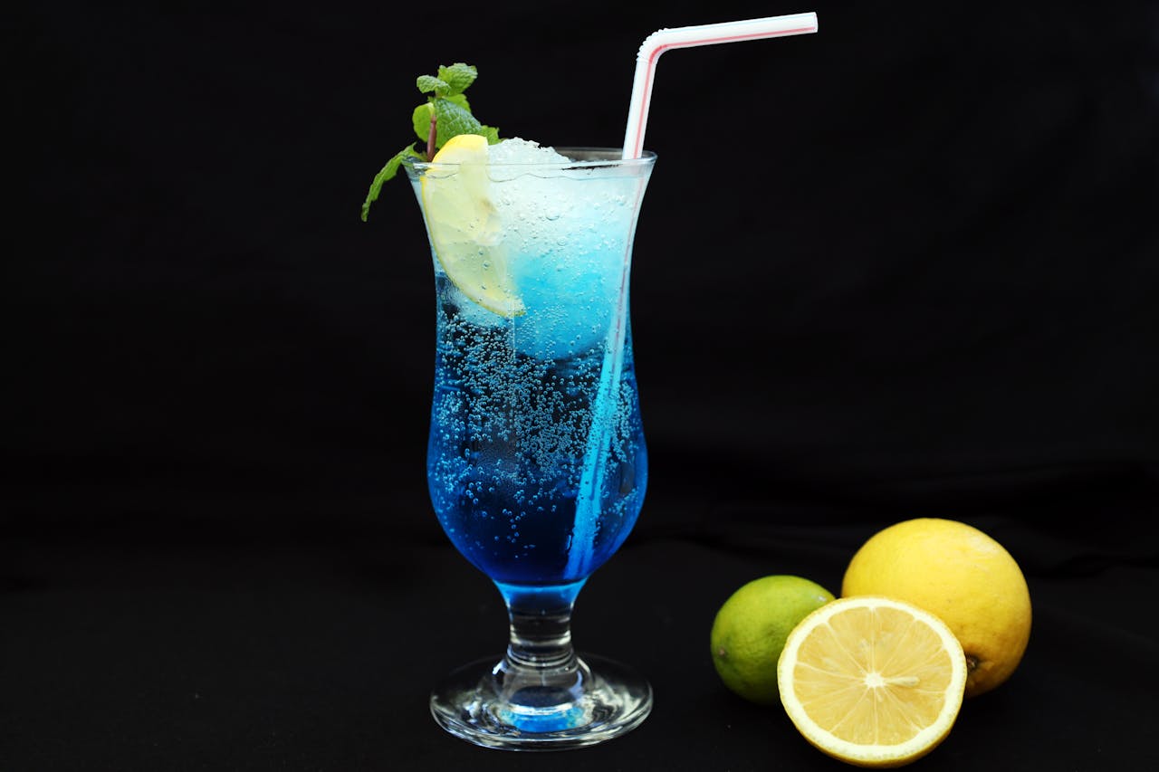 A vibrant blue cocktail with lemon and lime garnish on a black background, perfect for refreshment.
