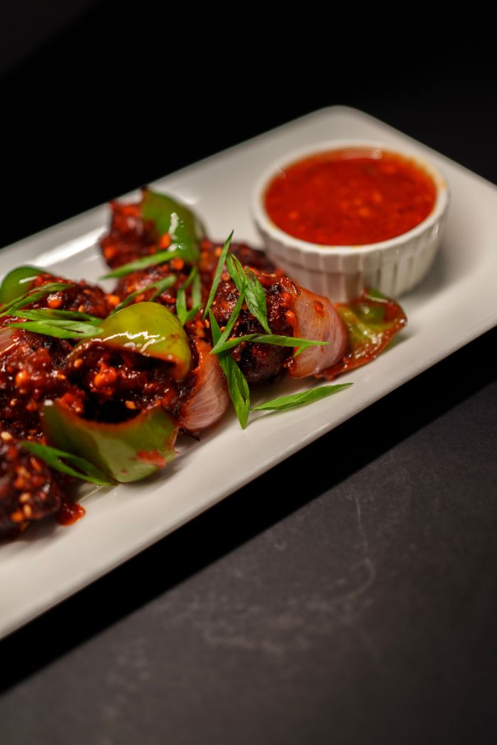about-us Close-up of spicy Indo-Chinese chilli chicken with sauce, garnished with spring onions.