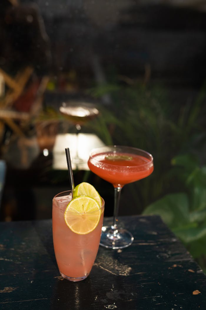Close-up of citrus and berry cocktails with lime garnish on a dark surface.