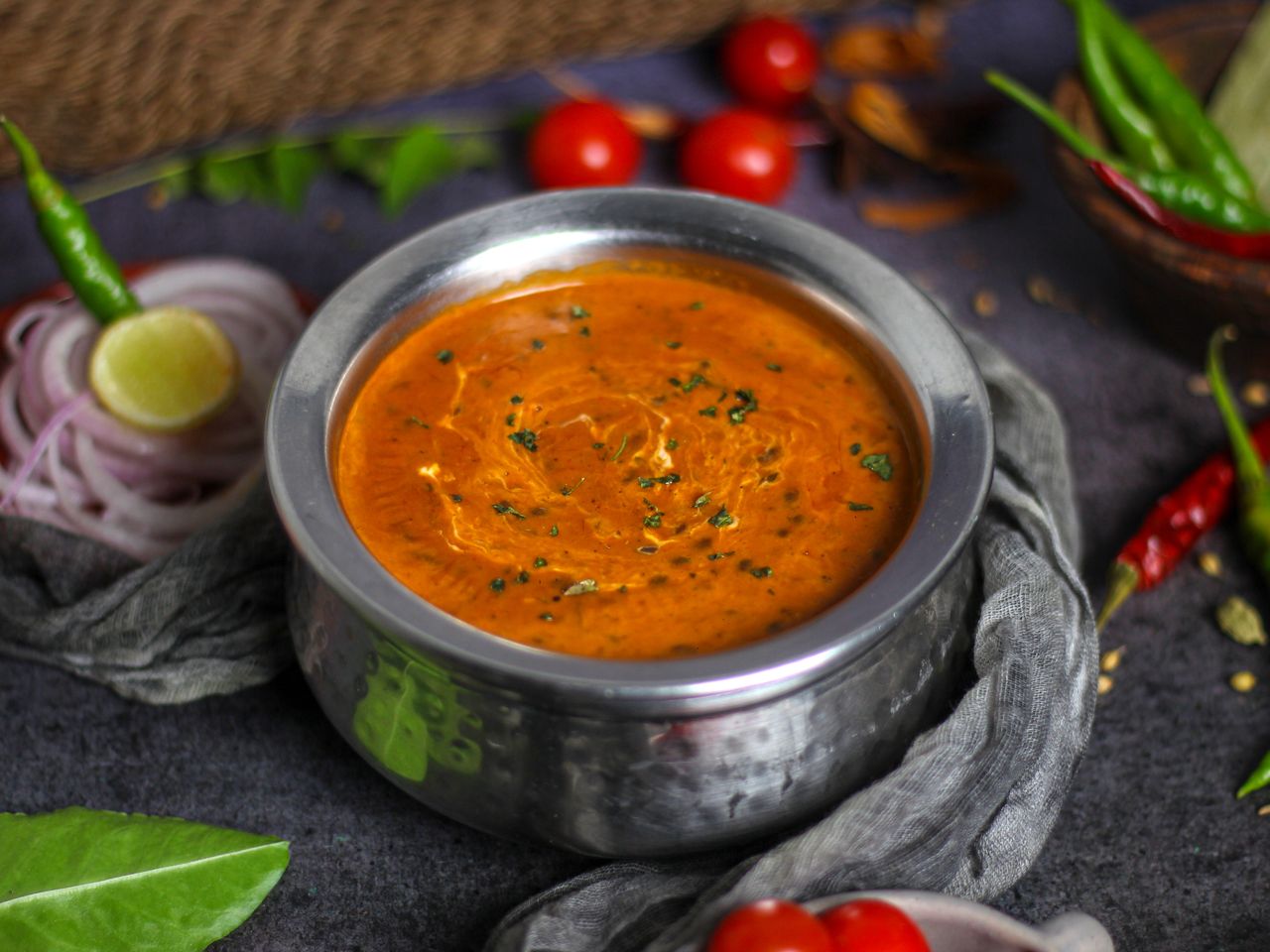 Rich and aromatic Indian curry with herbs and spices in a stainless steel bowl, surrounded by fresh ingredients.